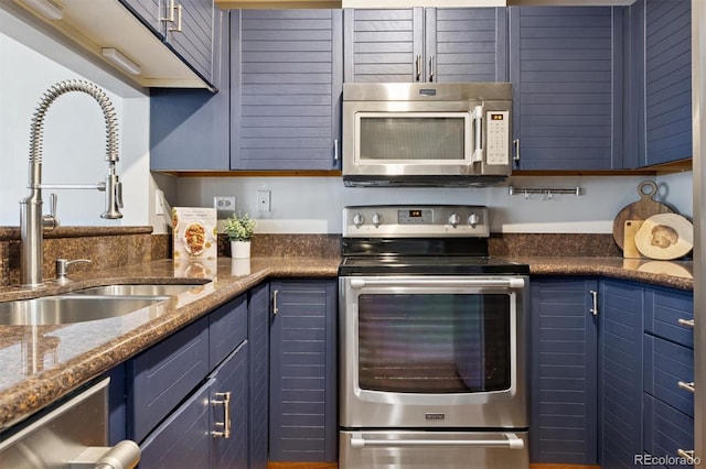 kitchen with dark stone countertops, blue cabinets, appliances with stainless steel finishes, and a sink