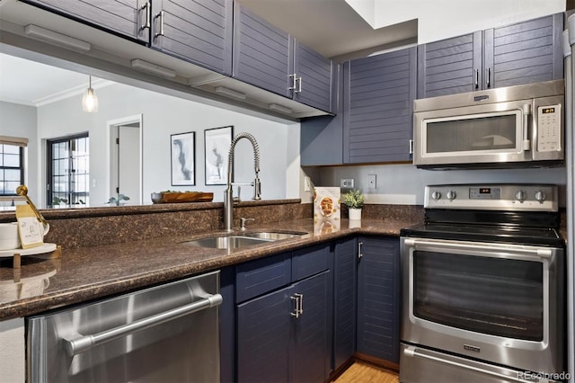 kitchen with a sink, blue cabinetry, dark stone counters, appliances with stainless steel finishes, and crown molding