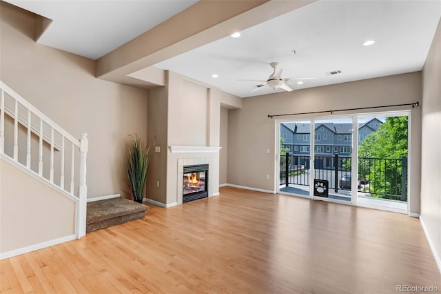 2763 W Riverwalk Cir Unit B, Littleton, CO 80123 - unfurnished living room featuring wood finished floors, baseboards, a ceiling fan, stairway, and a tiled fireplace