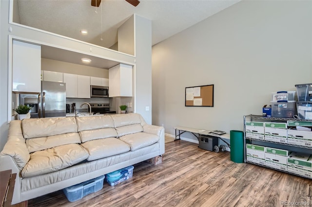 living room featuring ceiling fan, high vaulted ceiling, wood-type flooring, sink, and a textured ceiling