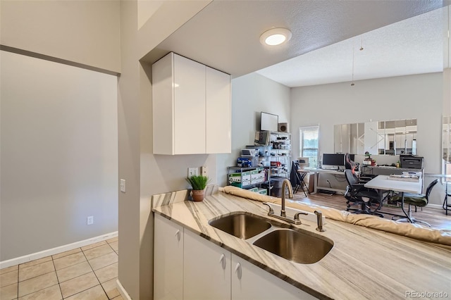 kitchen with sink, white cabinets, light stone countertops, and a towering ceiling