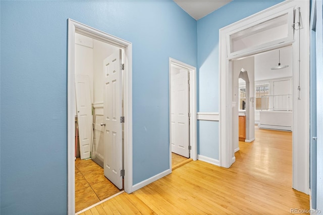 corridor featuring light wood-type flooring, baseboards, arched walkways, and baseboard heating