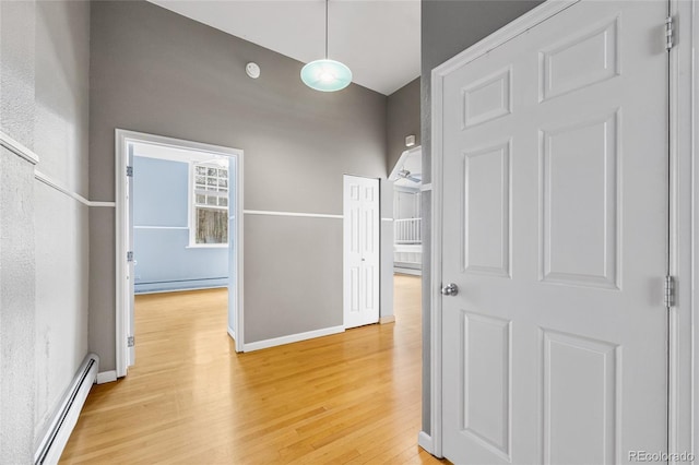 hall with light wood-type flooring, baseboards, a baseboard heating unit, and baseboard heating