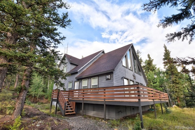 view of property exterior with a shingled roof, stairway, and a wooden deck