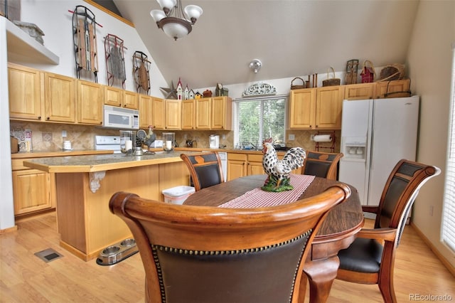 kitchen with light brown cabinets, white appliances, light wood-style floors, decorative backsplash, and a kitchen bar