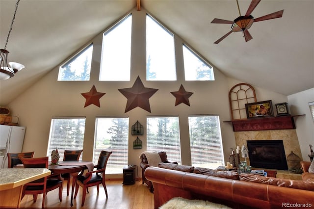 living area featuring a tile fireplace, a healthy amount of sunlight, light wood finished floors, and ceiling fan with notable chandelier