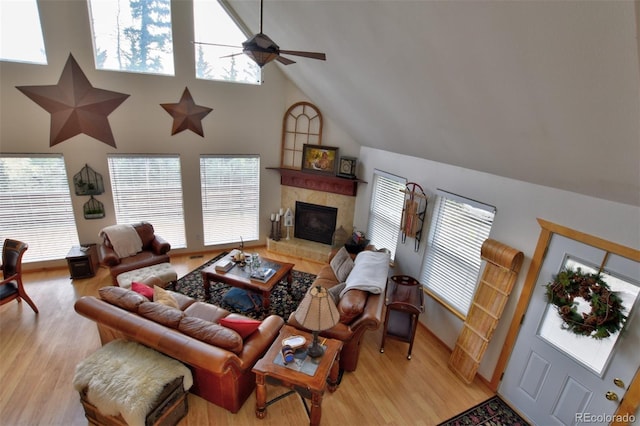 living room with a glass covered fireplace, ceiling fan, light wood-style flooring, and a high ceiling