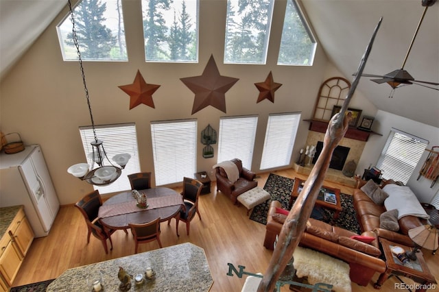 living area with a fireplace with raised hearth, ceiling fan with notable chandelier, a towering ceiling, and light wood-style flooring