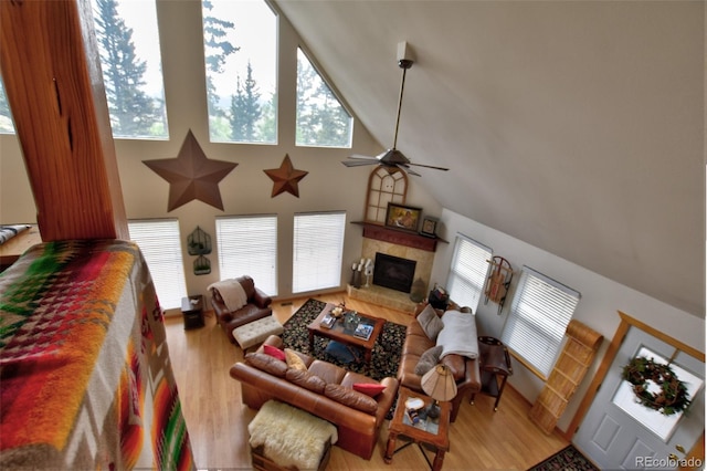 living area with a ceiling fan, a glass covered fireplace, high vaulted ceiling, and wood finished floors