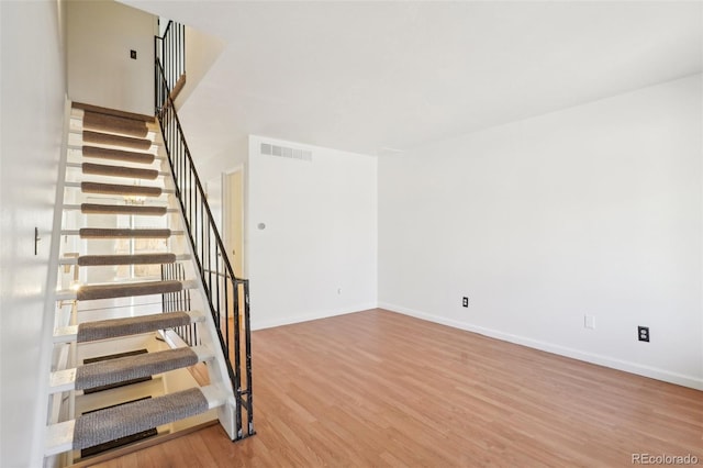 staircase with baseboards, visible vents, and wood finished floors