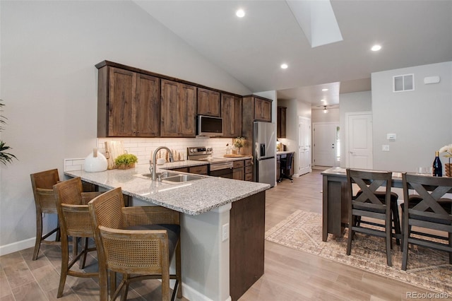 kitchen featuring sink, tasteful backsplash, light wood-type flooring, stainless steel appliances, and light stone countertops