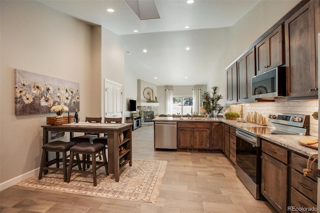 kitchen with kitchen peninsula, a stone fireplace, appliances with stainless steel finishes, tasteful backsplash, and light stone counters