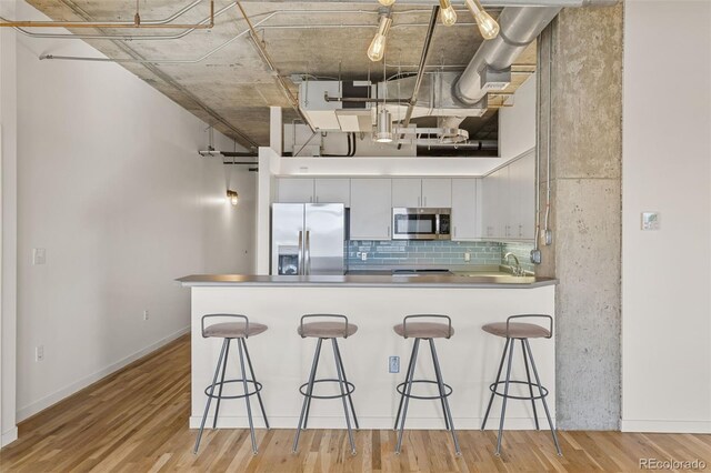 2020 Arapahoe St Unit 970, Denver, CO 80205 - kitchen with stainless steel appliances, a peninsula, decorative backsplash, a breakfast bar area, and light wood finished floors