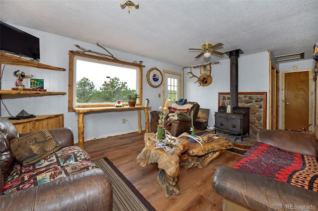 living room featuring a textured ceiling, ceiling fan, wood-type flooring, and a wood stove