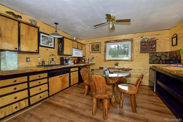 kitchen featuring wooden walls, sink, ceiling fan, hanging light fixtures, and dark hardwood / wood-style flooring