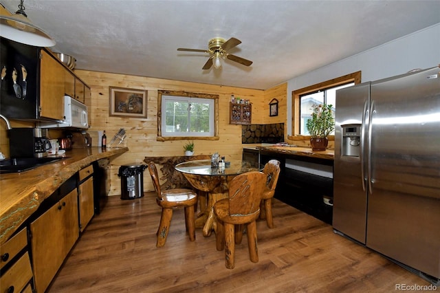 dining area with dark hardwood / wood-style flooring, sink, wood walls, and ceiling fan