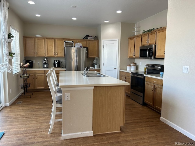 kitchen featuring wood-type flooring, appliances with stainless steel finishes, sink, and a kitchen island with sink