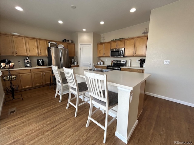 kitchen featuring appliances with stainless steel finishes, sink, a breakfast bar area, dark wood-type flooring, and a center island with sink