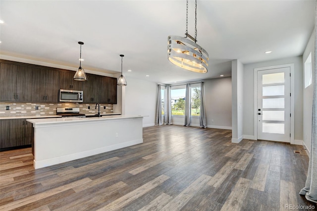 kitchen with decorative light fixtures, dark brown cabinets, wood-type flooring, appliances with stainless steel finishes, and decorative backsplash