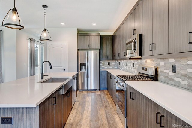 kitchen featuring a kitchen island with sink, light hardwood / wood-style flooring, backsplash, hanging light fixtures, and appliances with stainless steel finishes