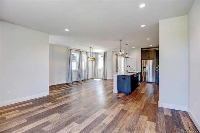 interior space with dark hardwood / wood-style floors, a center island with sink, pendant lighting, stainless steel fridge with ice dispenser, and sink