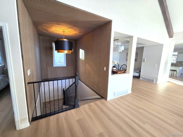 hall with beam ceiling, wooden walls, hardwood / wood-style floors, and a notable chandelier