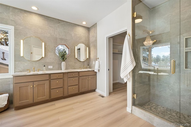 bathroom featuring hardwood / wood-style floors, vanity, a shower with door, and tile walls