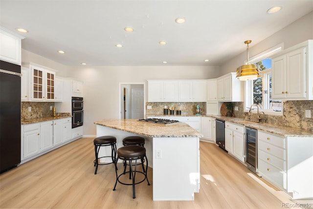 kitchen featuring sink, wine cooler, a kitchen island, light hardwood / wood-style floors, and white cabinetry