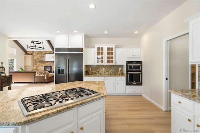 kitchen with tasteful backsplash, stainless steel appliances, white cabinets, light hardwood / wood-style floors, and a stone fireplace