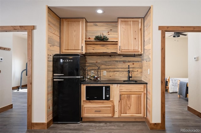 kitchen with dark wood-style floors, dark countertops, light brown cabinets, a sink, and black appliances