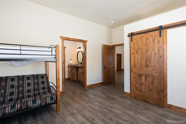 unfurnished bedroom featuring a barn door, ensuite bath, wood finished floors, and baseboards