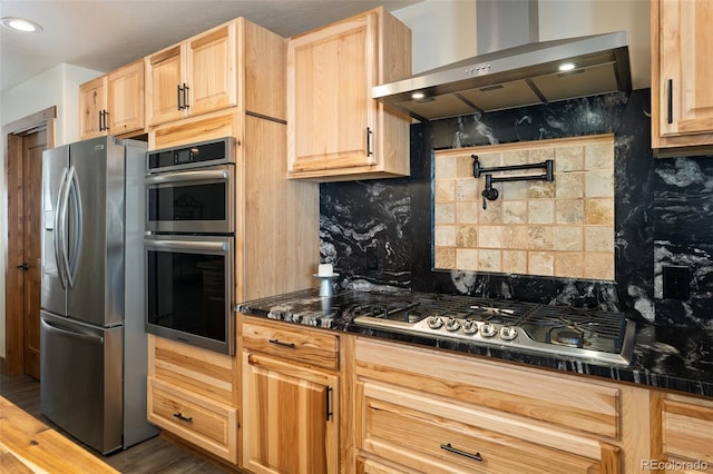 kitchen with stainless steel appliances, dark countertops, wall chimney exhaust hood, and light brown cabinetry