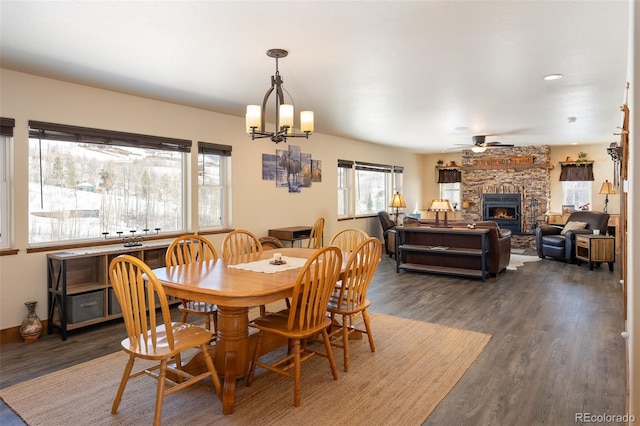 dining space featuring dark wood-style flooring, a fireplace, and ceiling fan with notable chandelier