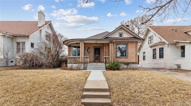 view of front of property featuring a front yard, covered porch, brick siding, and a chimney