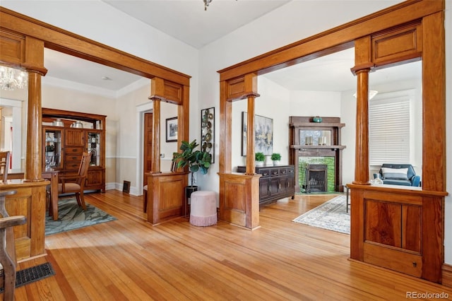 entrance foyer featuring decorative columns, a fireplace, visible vents, light wood-style flooring, and baseboards