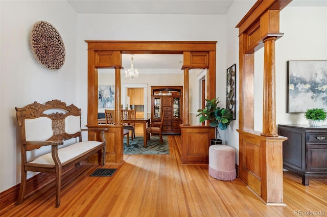 sitting room with ornate columns, light wood-style flooring, and a chandelier