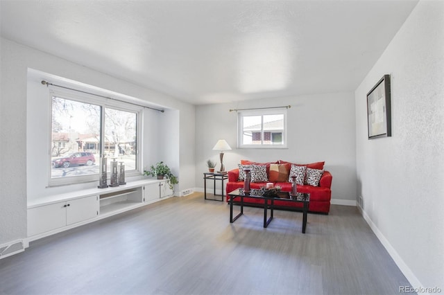 living area featuring a textured wall, wood finished floors, visible vents, and baseboards