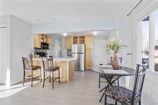 kitchen with tasteful backsplash, freestanding refrigerator, light brown cabinetry, black microwave, and open shelves