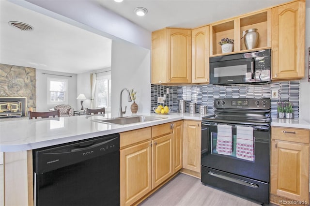 kitchen featuring light brown cabinets, a peninsula, a sink, visible vents, and black appliances