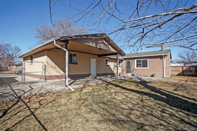 rear view of property featuring a patio, brick siding, fence, a yard, and a gate