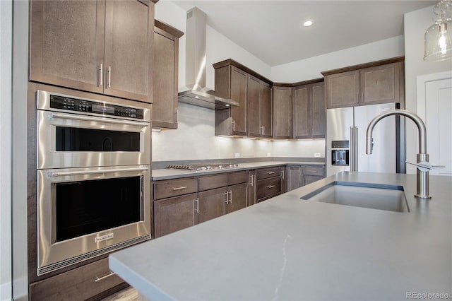 kitchen featuring wall chimney range hood, sink, dark brown cabinetry, and stainless steel appliances