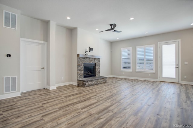 unfurnished living room featuring ceiling fan, light hardwood / wood-style floors, and a stone fireplace