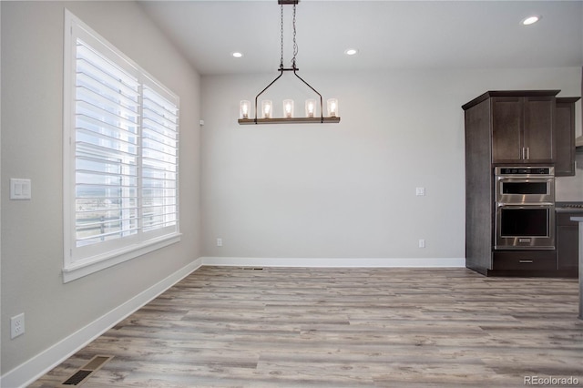 unfurnished dining area featuring an inviting chandelier, plenty of natural light, and light wood-type flooring