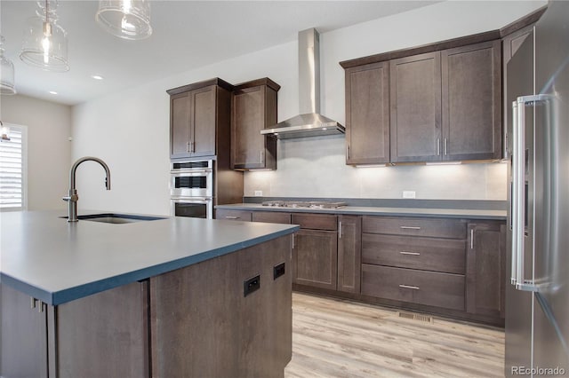 kitchen with light hardwood / wood-style floors, sink, appliances with stainless steel finishes, wall chimney range hood, and pendant lighting