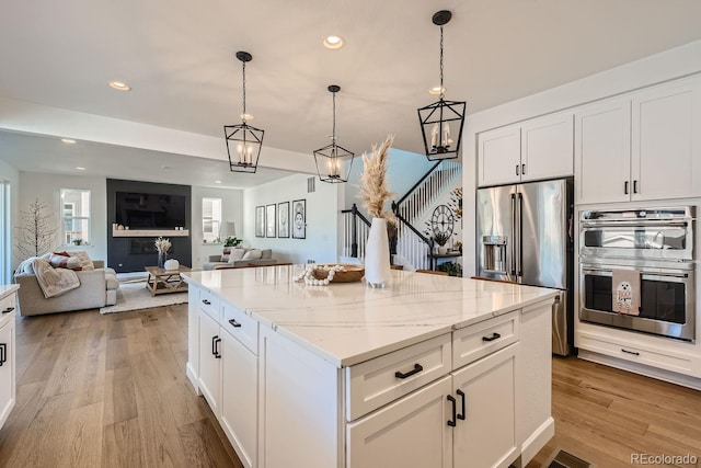 kitchen with decorative light fixtures, white cabinets, a center island, light stone counters, and stainless steel appliances