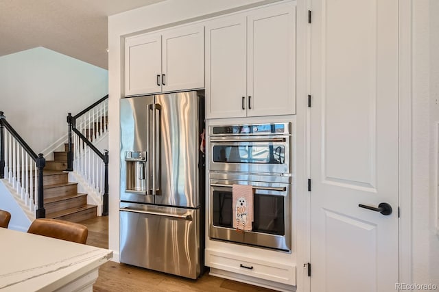 kitchen with stainless steel appliances, light hardwood / wood-style floors, and white cabinets