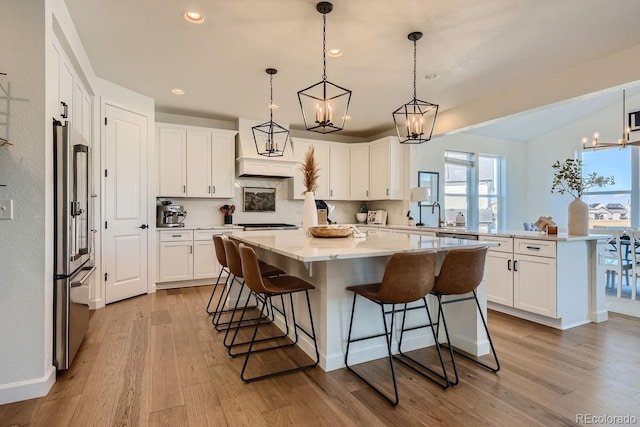 kitchen featuring a breakfast bar, decorative light fixtures, white cabinets, a center island, and high end fridge