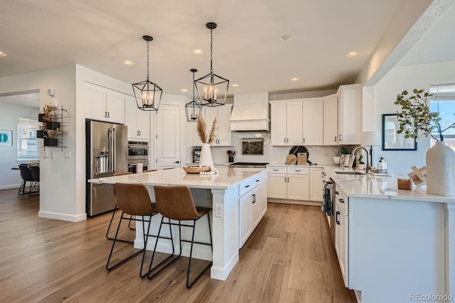 kitchen with a kitchen island, appliances with stainless steel finishes, decorative light fixtures, white cabinets, and custom range hood