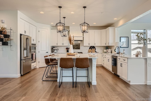 kitchen with light hardwood / wood-style flooring, white cabinetry, a kitchen island, stainless steel appliances, and a kitchen bar