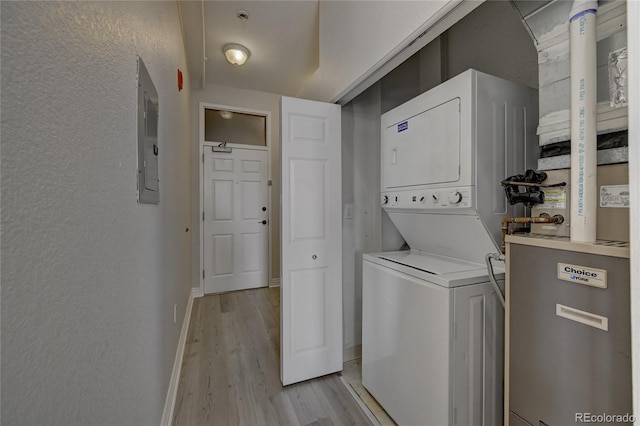 laundry area featuring a textured wall, stacked washer and dryer, laundry area, baseboards, and light wood-type flooring